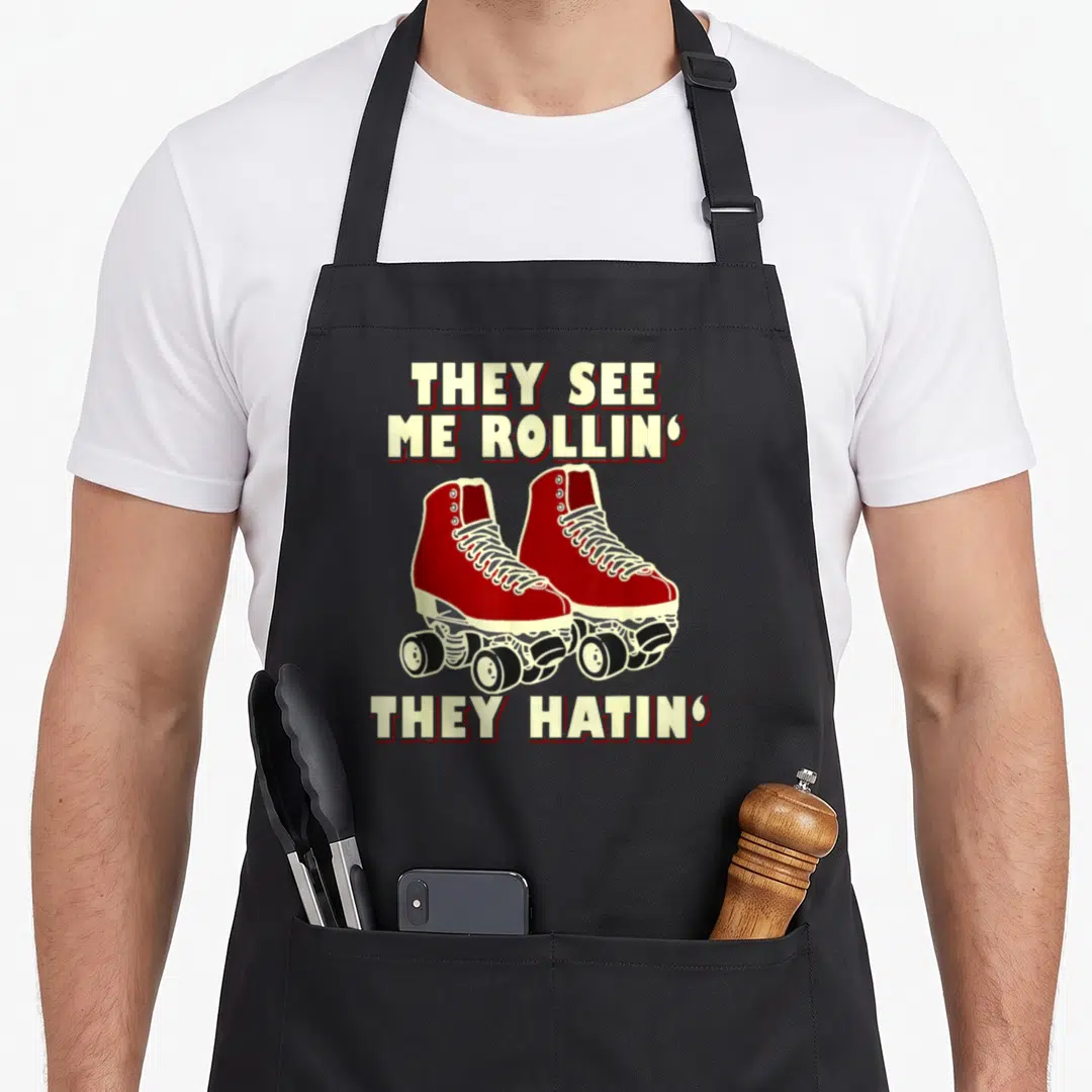 Skating see me aprons - Red quad skates with THEY SEE ME ROLLIN THEY HATIN text — shown on a black cotton canvas apron against a white background