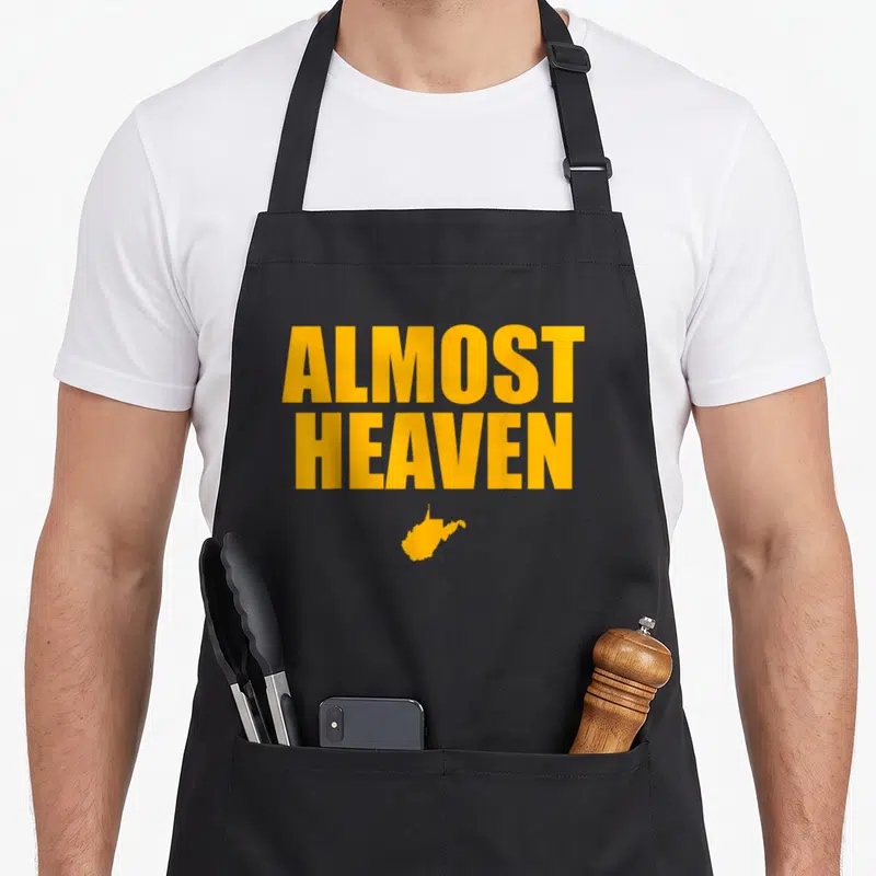 Almost virginia girl apron - Yellow ALMOST HEAVEN text above a West Virginia state map silhouette — shown on a black cotton canvas apron against a white background