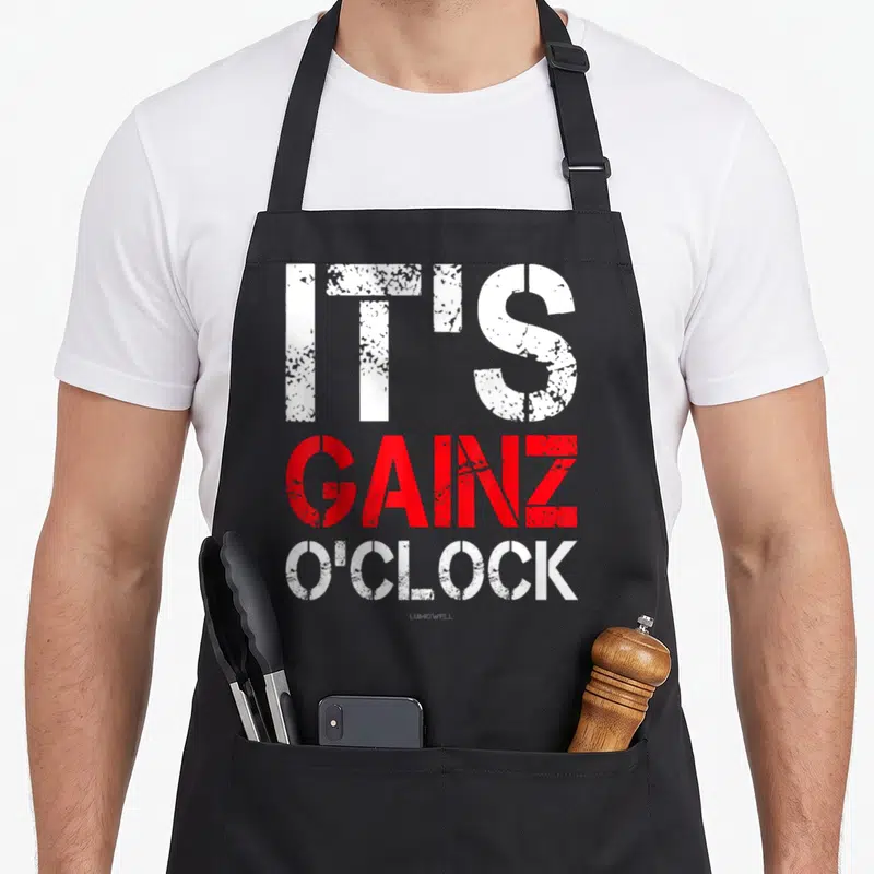 Bodybuilding gains apron - Stacked white and red text reading It's Gainz O'Clock in distressed font — shown on a black cotton canvas apron against a white background