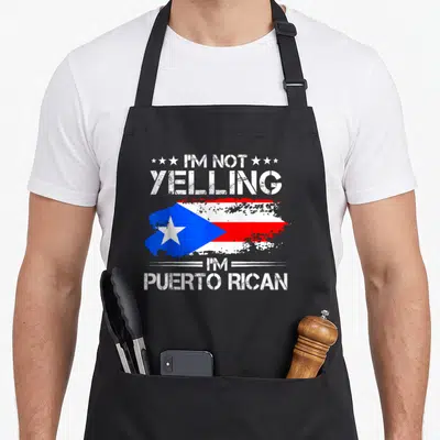 Yelling puerto pride apron - Distressed Puerto Rican flag with white text I'm Not Yelling I'm Puerto Rican — shown on a black cotton canvas apron against a white background