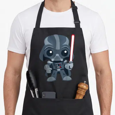 Saber cartoon apron - Cartoon Darth Vader holding red lightsaber in grey white and red — shown on a black cotton canvas apron against a white background