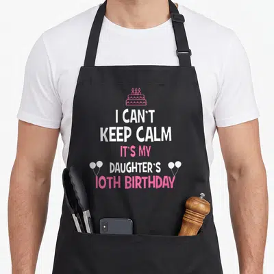 Daughter 10th birthday apron - Pink cake and white balloons flanking stacked text celebrating a tenth birthday — shown on a black cotton canvas apron against a white background