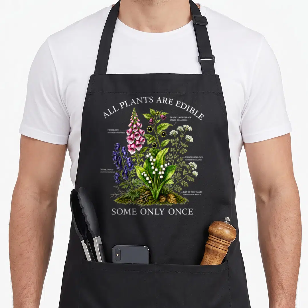 Botanical plant apron - All Plants Are Edible Some Only Once text surrounding toxic botanical illustrations in green — shown on a black cotton canvas apron against a white background