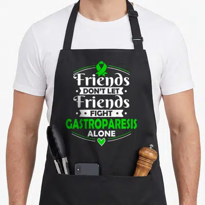 Stomach gastroparesis awareness apron - Green ribbon and heart with stacked white and green text reading Friends Don't — shown on a black cotton canvas apron against a white background