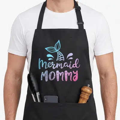 Family mama apron - Mermaid tail with blue purple pink splashes and mermaid MOMMY text in cartoon style — shown on a black cotton canvas apron against a white background