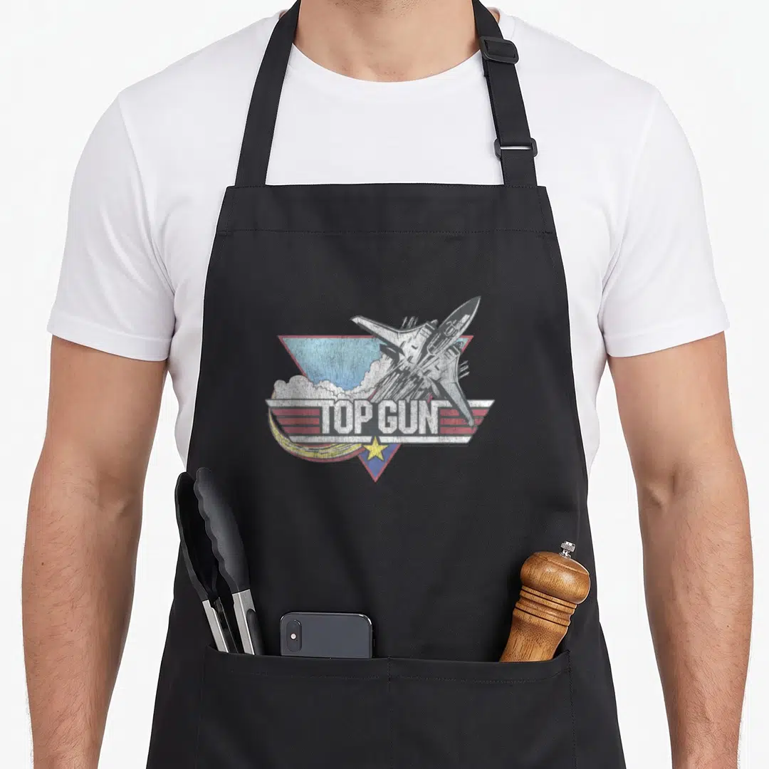 Funny jet gun apron - Distressed TOP GUN fighter jet graphic with yellow star and red stripes on black apron — shown on a black cotton canvas apron against a white background