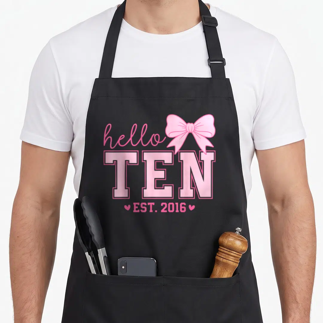 Hello bow apron - Pink hello TEN EST 2016 text with bow and two hearts — shown on a black cotton canvas apron against a white background