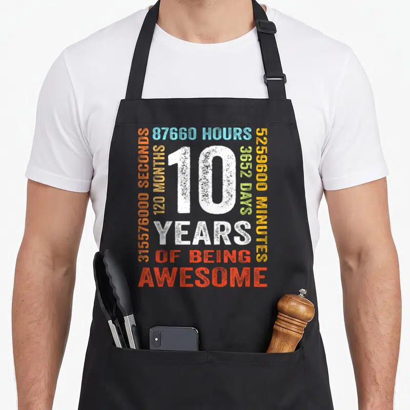 10th month birthday apron - White 10 surrounded by colored time stats and Years of Being Awesome text — shown on a black cotton canvas apron against a white background