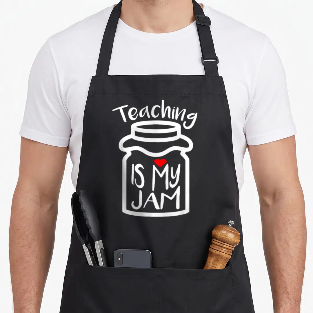 Teaching jam teacher apron - White outline of a jam jar with text Teaching IS MY JAM and a red heart — shown on a black cotton canvas apron against a white background