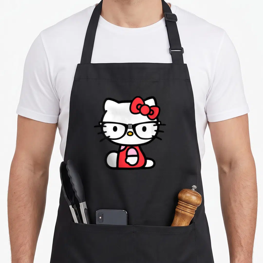Funny glass nerd apron - Hello Kitty cartoon wearing black glasses and red bow on white background — shown on a black cotton canvas apron against a white background