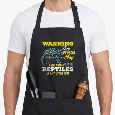 Reptile uab kidkis apron - Floral chameleon silhouette with warning text about talking about reptiles and three hearts — shown on a black cotton canvas apron against a white background