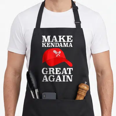 Kendama fan gear apron - Red baseball cap with two crossed kendamas and white slogan text — shown on a black cotton canvas apron against a white background