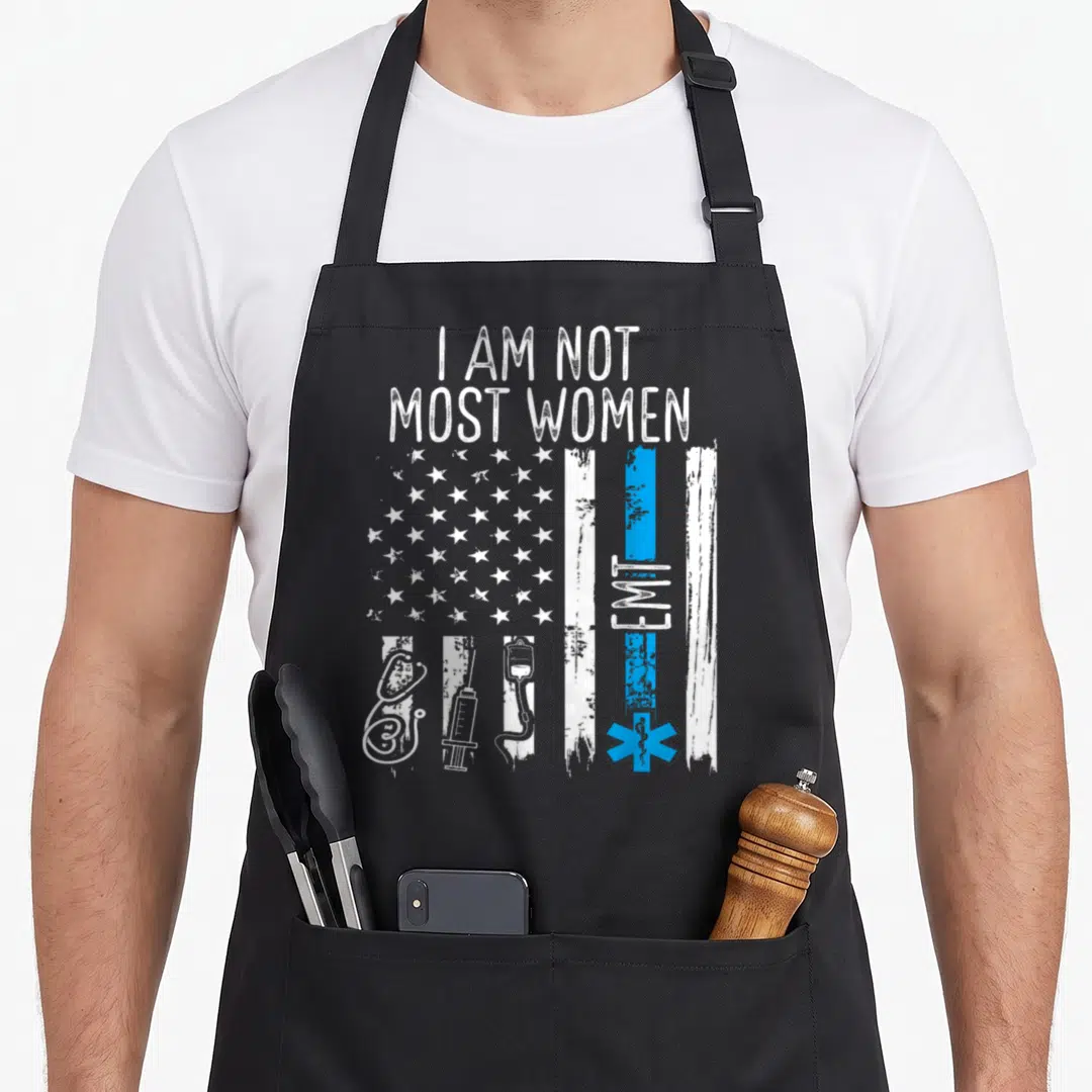Emt healthcare apron - Distressed flag with I AM NOT MOST WOMEN text and medical equipment stripes in white and blue — shown on a black cotton canvas apron against a white background