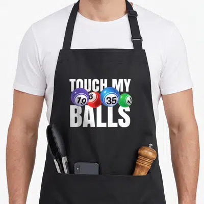 Touch bingo aprons - TOUCH MY BALLS text with four numbered bingo balls in purple red blue green — shown on a black cotton canvas apron against a white background