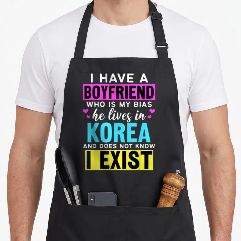 Boyfriend korean apron - Typography design reading I Have A Boyfriend Who Is My Bias He Lives In Korea And Does Not — shown on a black cotton canvas apron against a white background