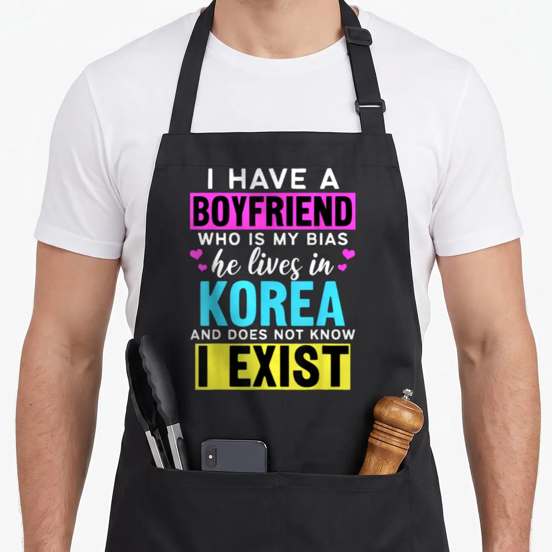 Boyfriend korean apron - Typography design reading I Have A Boyfriend Who Is My Bias He Lives In Korea And Does Not — shown on a black cotton canvas apron against a white background