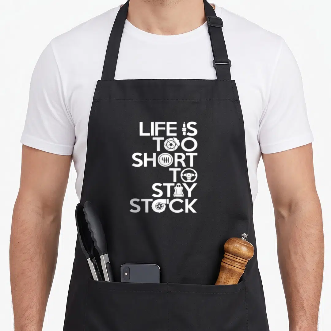 Classical stock aprons - White stacked text LIFE IS TOO SHORT TO STAY STOCK with car part icons replacing letters — shown on a black cotton canvas apron against a white background