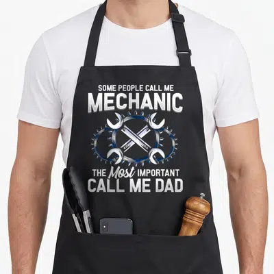 Styley mechanic apron - White and blue crossed wrenches in gear border with text about mechanic and dad — shown on a black cotton canvas apron against a white background