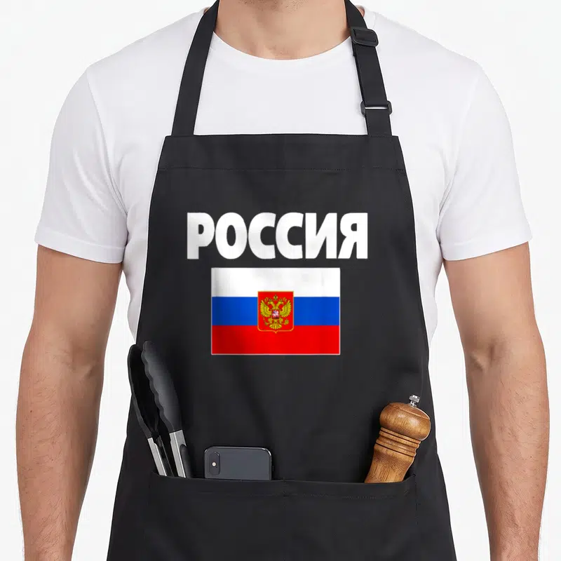 Poccna russian apron - Cyrillic Rossiya text above white blue red Russian flag with golden double-headed eagle emblem — shown on a black cotton canvas apron against a white background