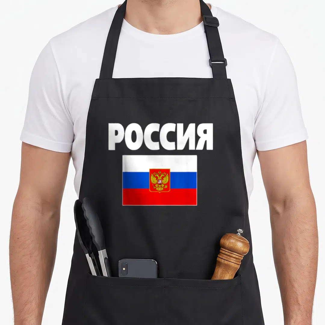 Poccna russian apron - Cyrillic Rossiya text above white blue red Russian flag with golden double-headed eagle emblem — shown on a black cotton canvas apron against a white background