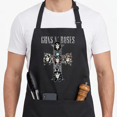 Rose skull gun apron - GUNS N' ROSES text above four skulls in a cross formation with hats and sunglasses — shown on a black cotton canvas apron against a white background