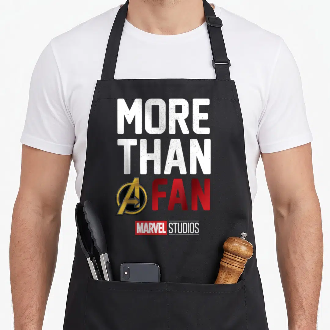 Studio novelty apron - Stacked More Than A Fan text with Avengers logo replacing A and Marvel Studios logo below — shown on a black cotton canvas apron against a white background