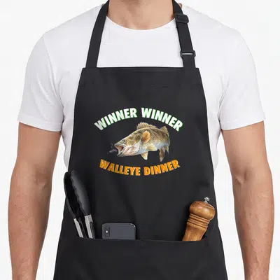 Funny fish fry apron - Realistic walleye with lure and arched text Winner Winner Walleye Dinner in green orange gold — shown on a black cotton canvas apron against a white background