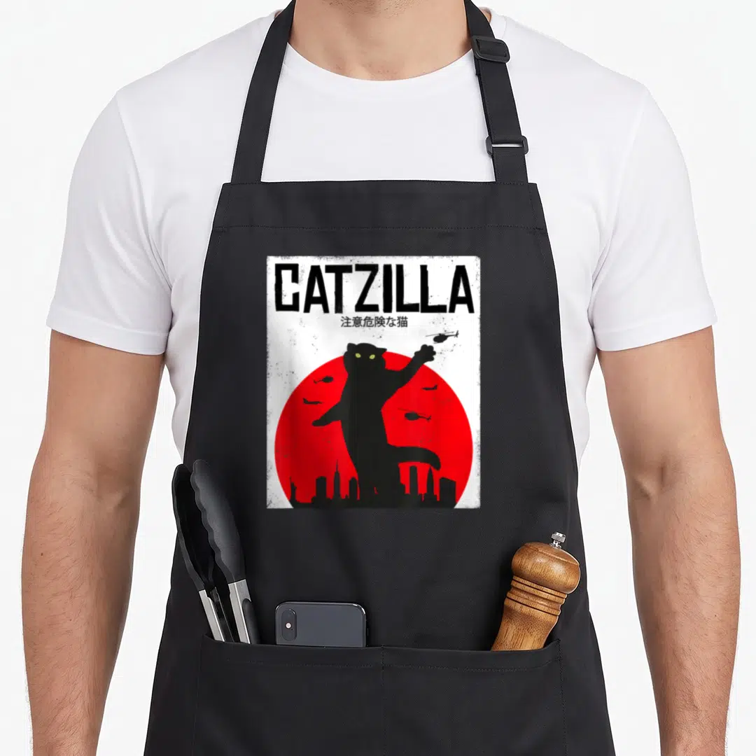 Catzilla japan apron - Black cat silhouette over red sun with CATZILLA text and flying aircraft — shown on a black cotton canvas apron against a white background