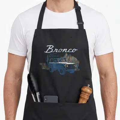 Ford outdoor apron - Distressed Bronco Ford lettering over blue car, cacti, and mountains in desert colors — shown on a black cotton canvas apron against a white background