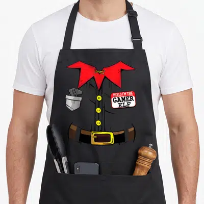 Stocking christmas elf apron - Cartoon elf torso with controller pocket and HELLO I'M THE GAMER ELF name tag — shown on a black cotton canvas apron against a white background
