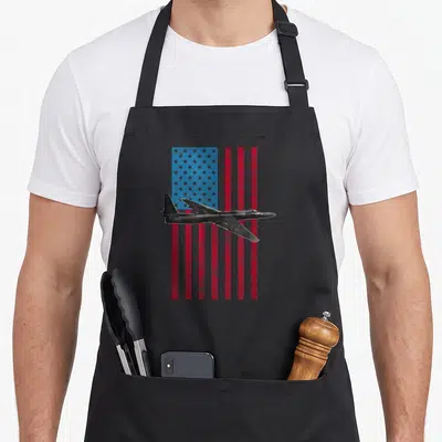 Dragon american flag apron - Black jet flying over distressed red white and blue stars and stripes flag — shown on a black cotton canvas apron against a white background