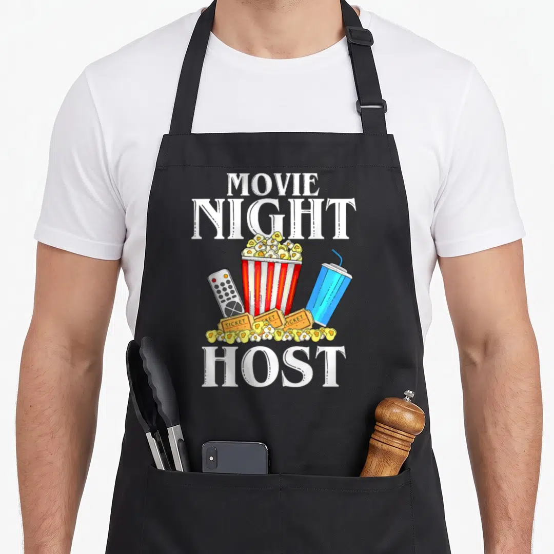 Night outfit family aprons - Cartoon popcorn bucket, tickets, remote, and drink between white MOVIE NIGHT HOST text — shown on a black cotton canvas apron against a white background