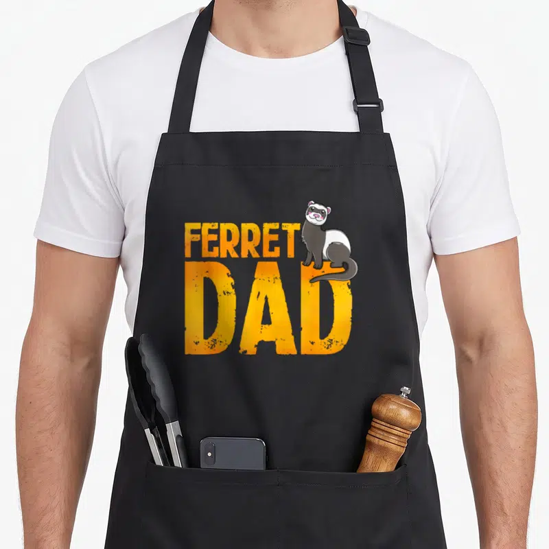Rodent daddy apron - Cartoon ferret sitting on orange FERRET DAD text in grey and white — shown on a black cotton canvas apron against a white background
