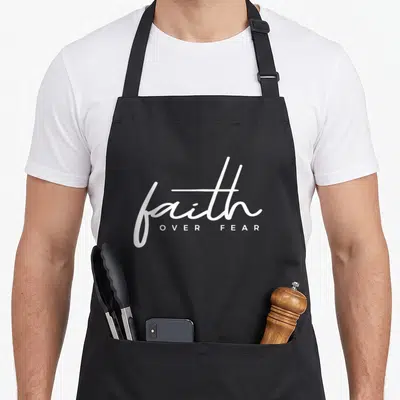 Vintage faith christian apron - White script faith above block letters OVER FEAR on black background — shown on a black cotton canvas apron against a white background