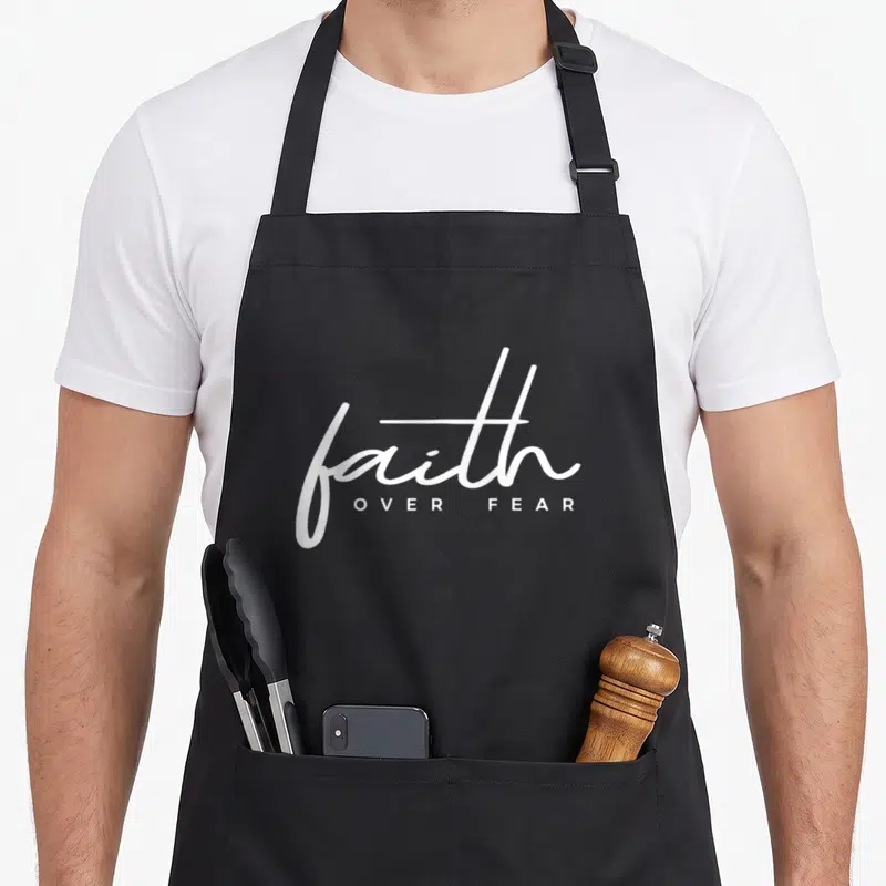 Vintage faith christian apron - White script faith above block letters OVER FEAR on black background — shown on a black cotton canvas apron against a white background
