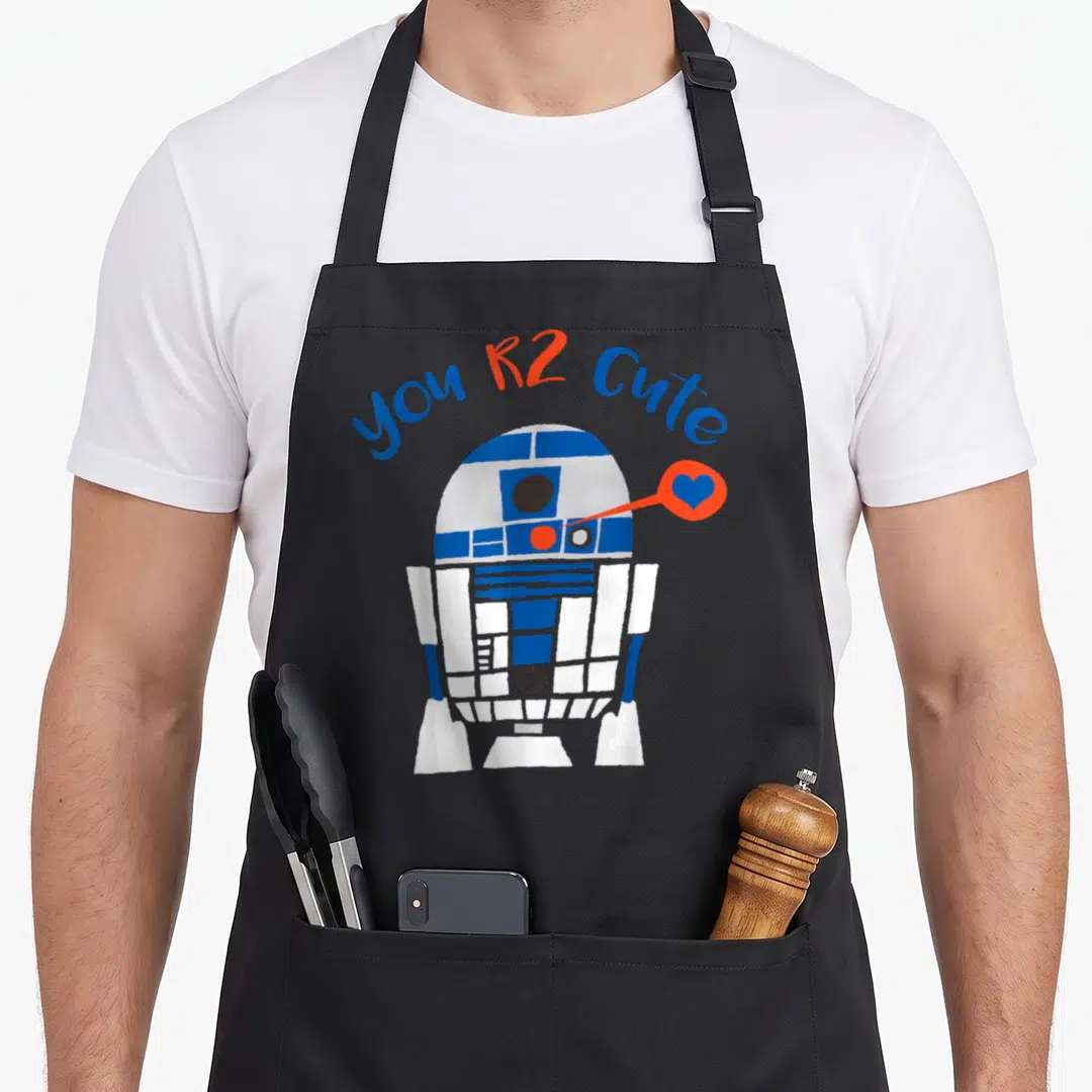 Cool valentine's day apron - you R2 Cute text arching over cartoon R2-D2 with blue heart in orange bubble — shown on a black cotton canvas apron against a white background