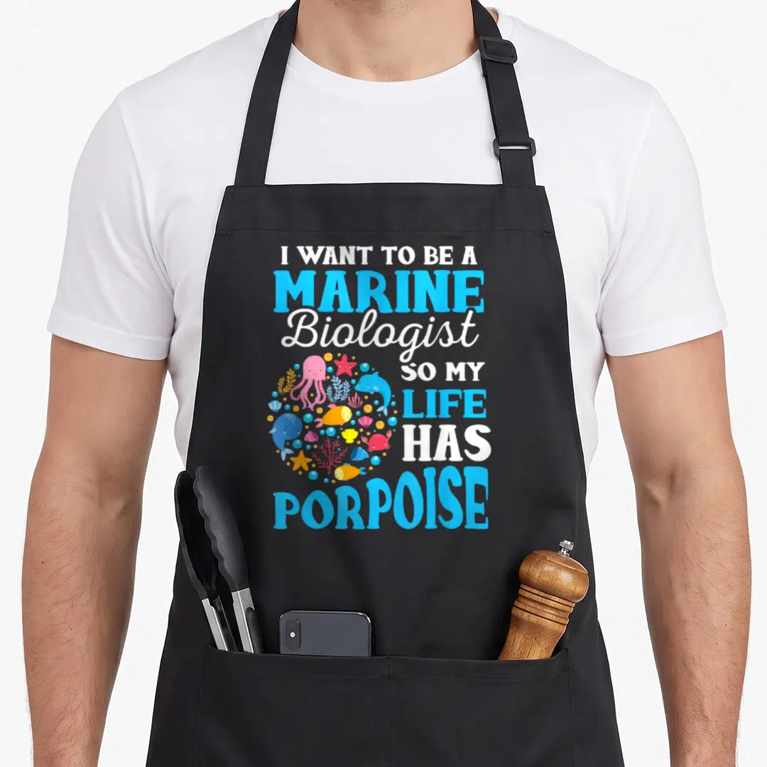 Biology marine biologist apron - I WANT TO BE A MARINE Biologist SO MY LIFE HAS PORPOISE text with circular sea — shown on a black cotton canvas apron against a white background