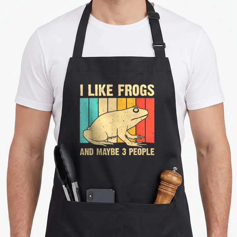 Toad amphibian frog aprons - Retro beige frog on teal yellow orange red stripes with text about liking frogs and few — shown on a black cotton canvas apron against a white background