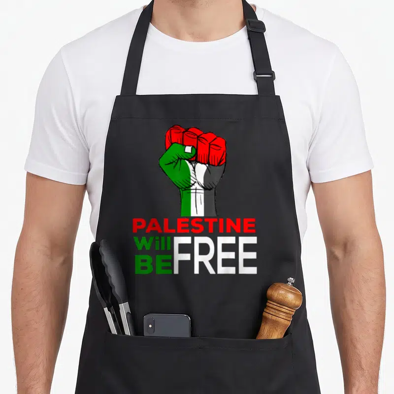 Flag palestine apron - Raised fist in red green white black above stacked text PALESTINE Will BE FREE — shown on a black cotton canvas apron against a white background