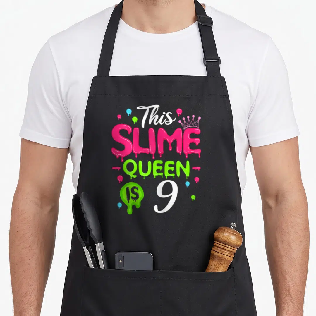 Slime birthday queen apron - Text This SLIME QUEEN IS 9 with pink dripping letters green blob and crown — shown on a black cotton canvas apron against a white background