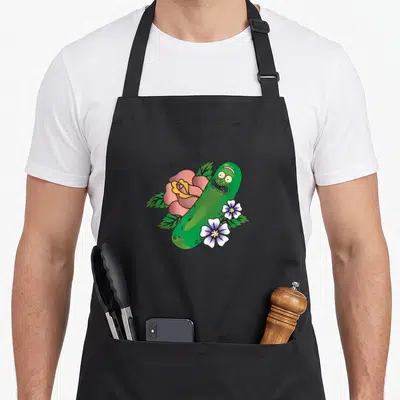 Tattoo pickle apron - Green cartoon pickle leaning on pink rose with arching text and small white flowers at base — shown on a black cotton canvas apron against a white background