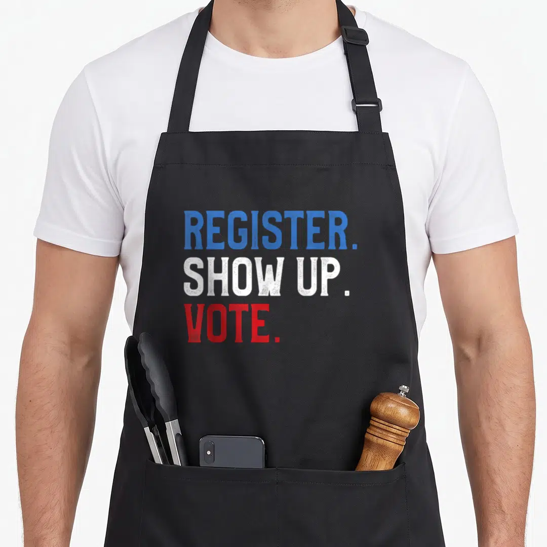 Voter midterms apron - Stacked blue, white, and red text reading REGISTER. SHOW UP. VOTE — shown on a black cotton canvas apron against a white background