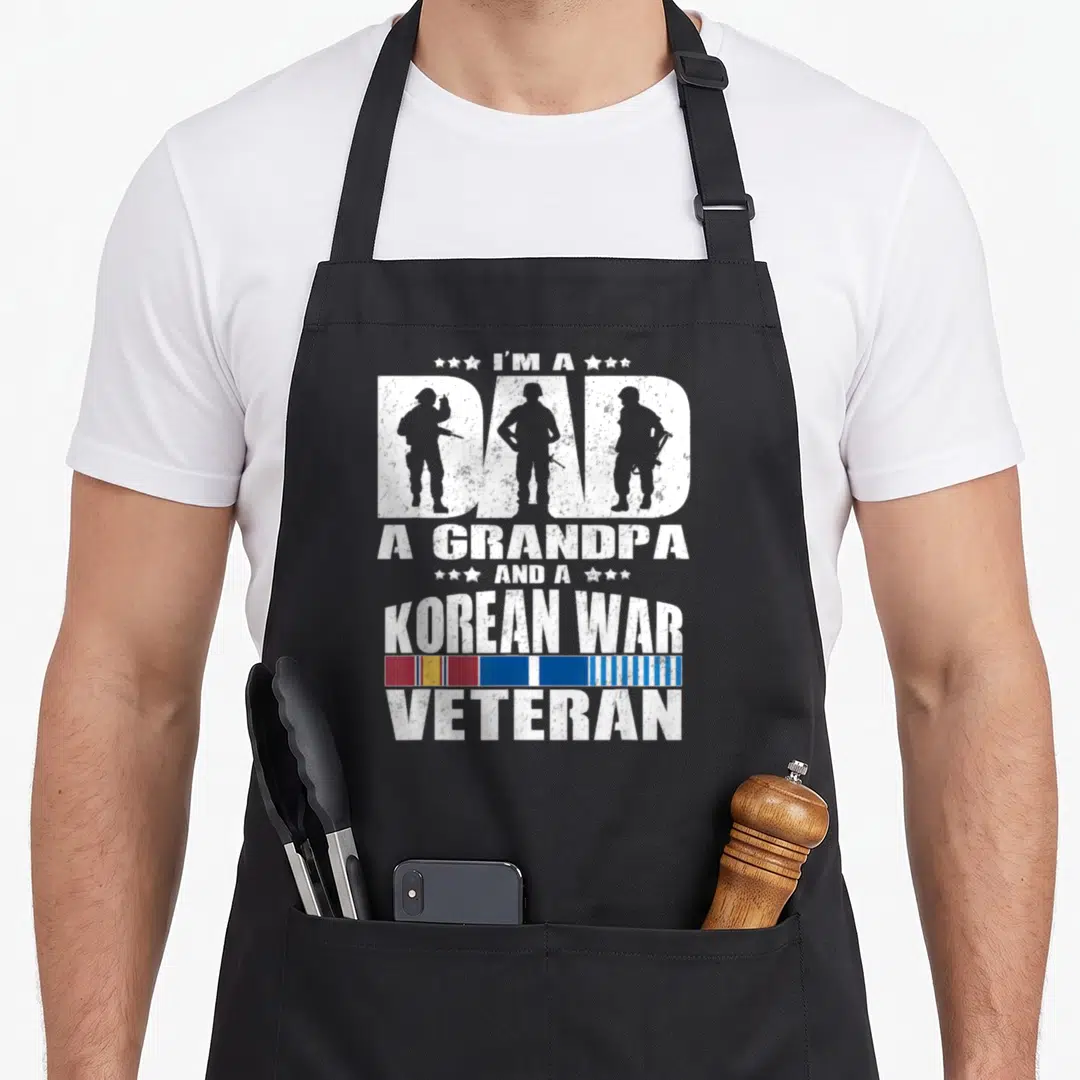 Grandpa korean apron - Stacked white text with soldier silhouettes inside DAD and multicolor ribbon below Korean War — shown on a black cotton canvas apron against a white background