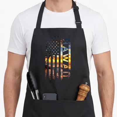 Hawaiian american flag apron - Vertical HAWAII text filled with sunset beach scene next to a grid of stars — shown on a black cotton canvas apron against a white background