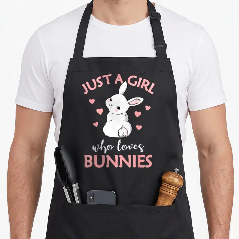 Funny rabbit bunny apron - White cartoon bunny with six pink hearts and text JUST A GIRL who loves BUNNIES — shown on a black cotton canvas apron against a white background