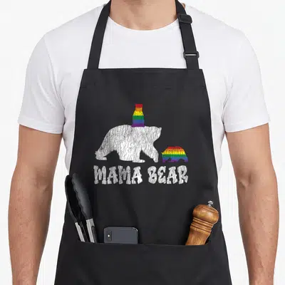 Lesbian cute bear apron - Distressed white bear with rainbow hat next to rainbow cub, MAMA BEAR text below — shown on a black cotton canvas apron against a white background