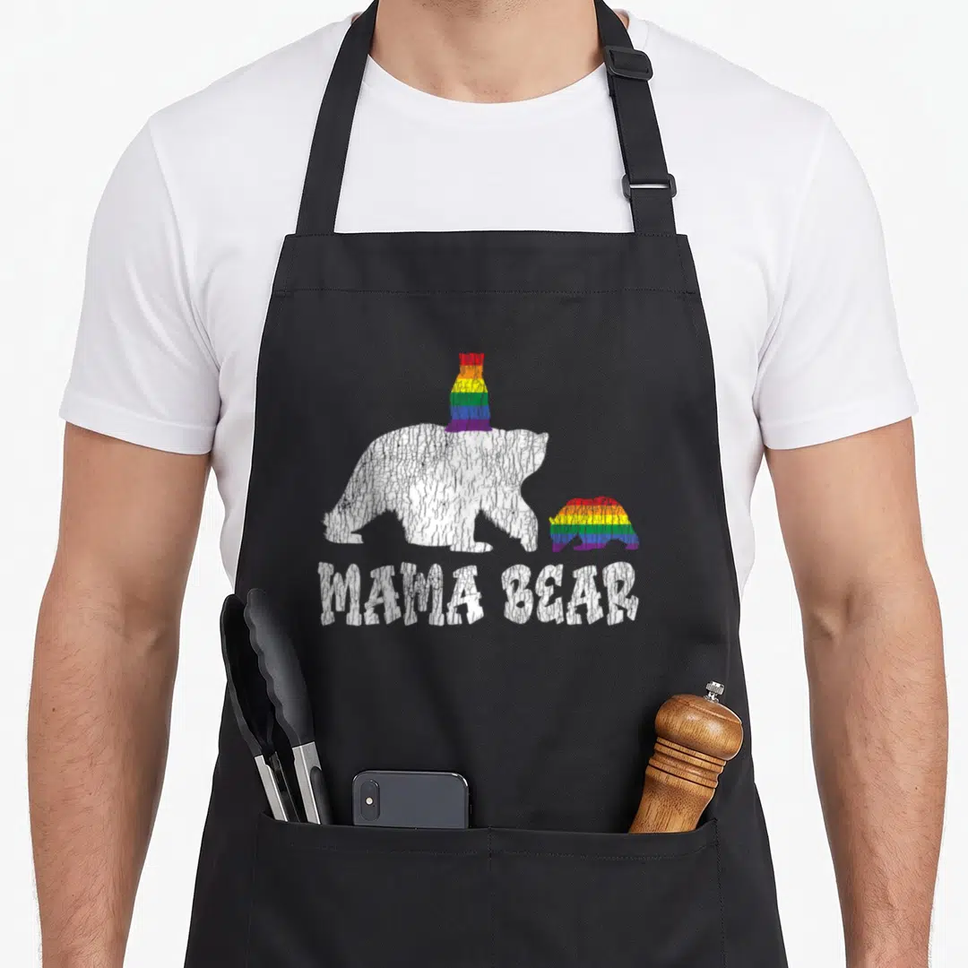 Lesbian cute bear apron - Distressed white bear with rainbow hat next to rainbow cub, MAMA BEAR text below — shown on a black cotton canvas apron against a white background