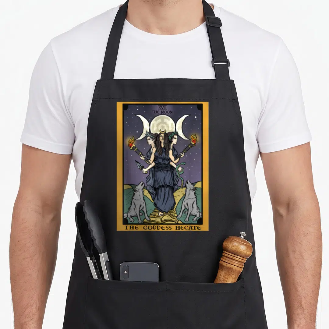 Goddess witch apron - Hecate triform holding torches flanked by two dogs under triple moon border — shown on a black cotton canvas apron against a white background