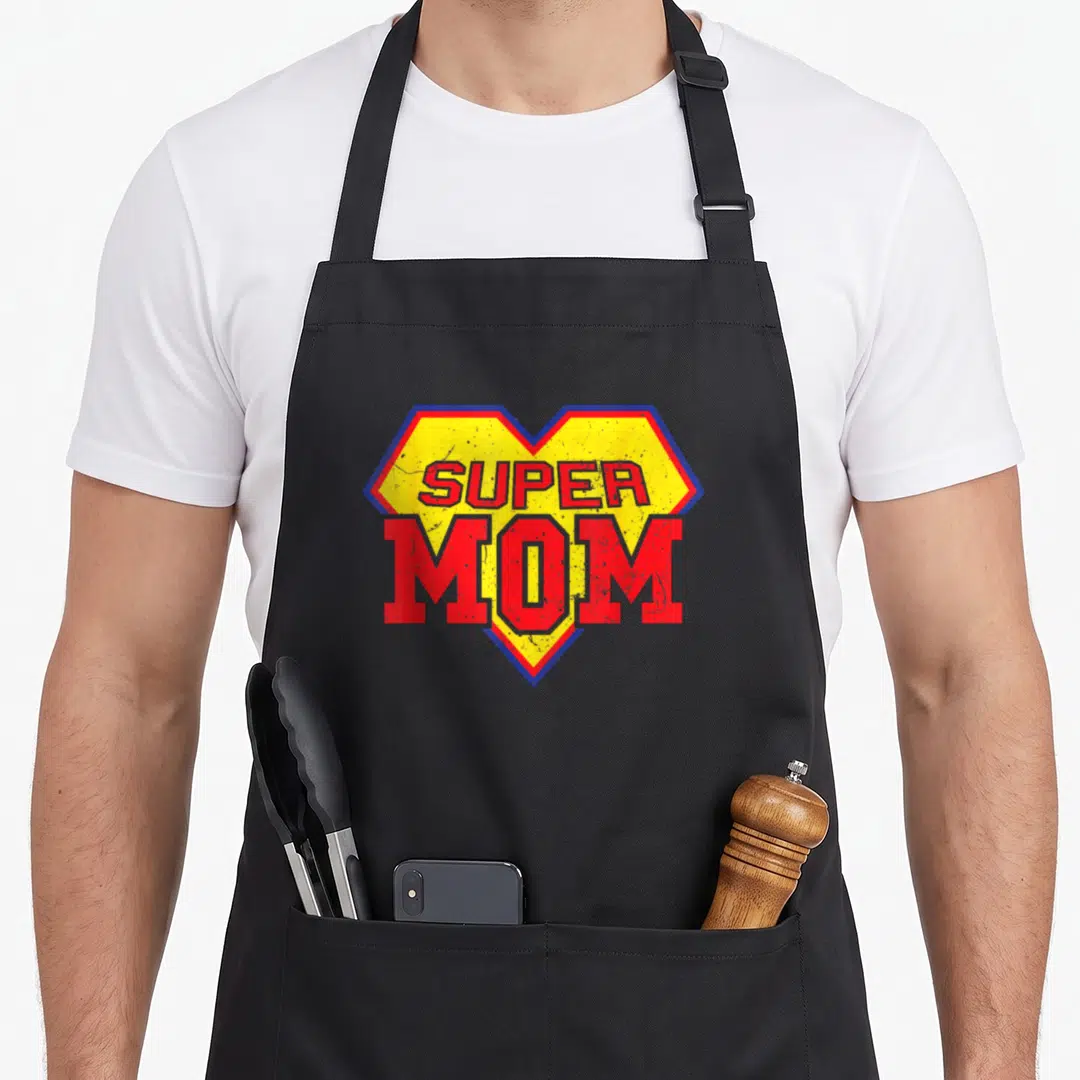 Superhero mummy and me aprons - Yellow shield with red blue border and distressed SUPER MOM text — shown on a black cotton canvas apron against a white background