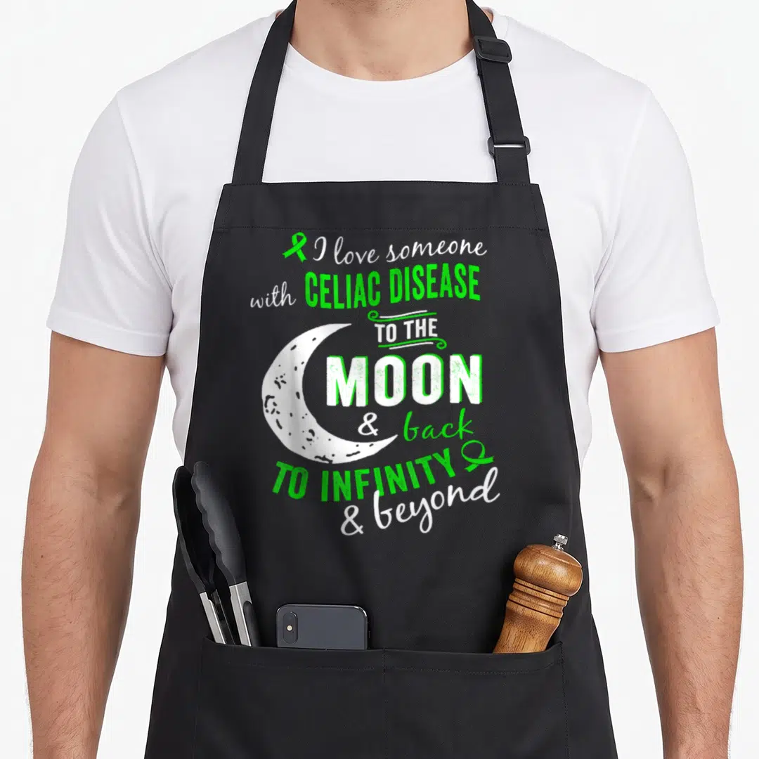 Cute disease celiac awareness apron - Green and white text around a crescent moon with awareness ribbons — shown on a black cotton canvas apron against a white background